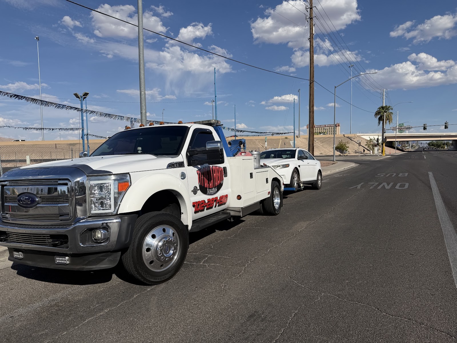White Ford tow truck towing a sedan on a Las Vegas street with blue sky