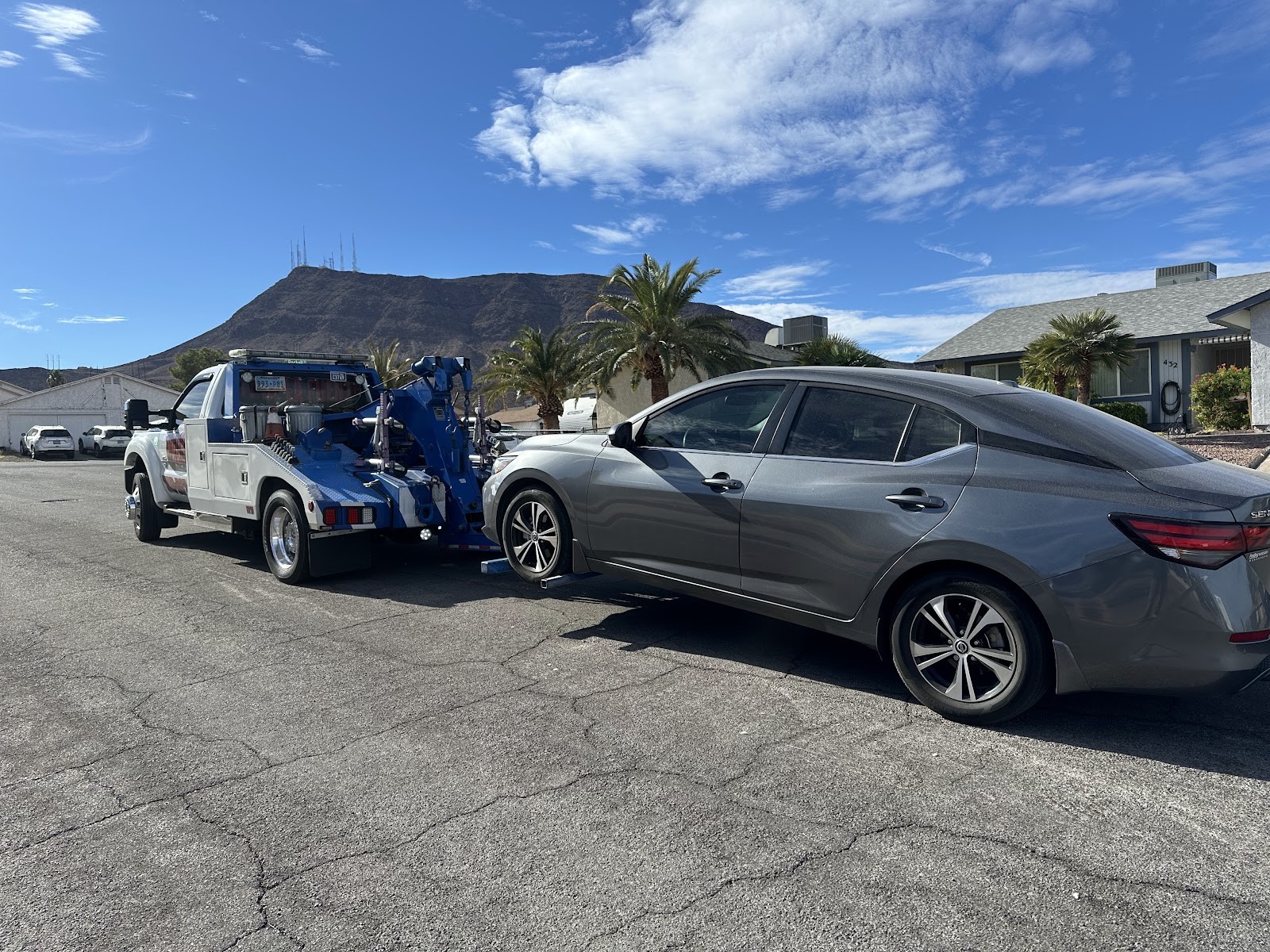 Tow truck wheel-lift towing a gray Nissan Sentra with mountain backdrop