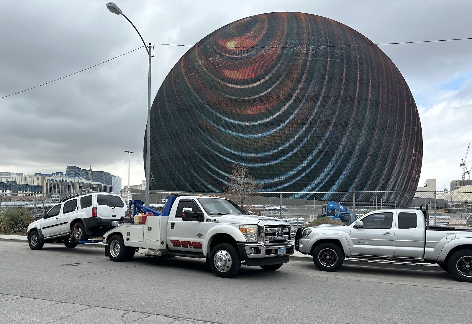 Ford tow truck with an SUV loaded in front of the Las Vegas Sphere